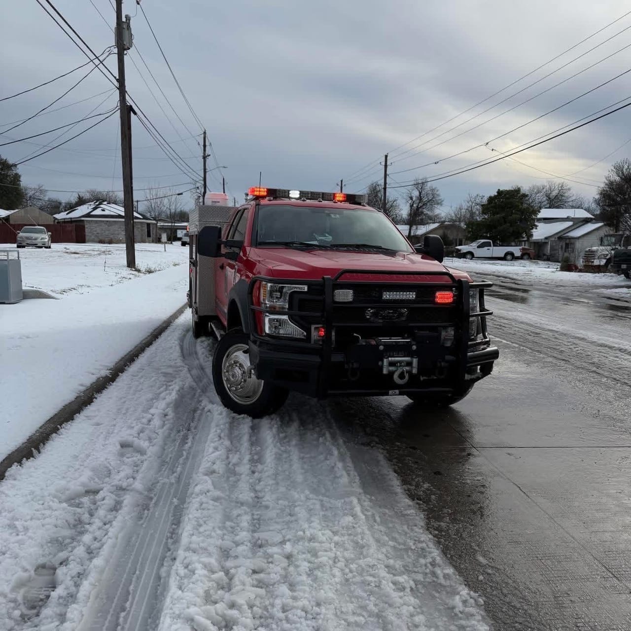 A red Cockrell Hill Fire Department pickup with emergency lights drives down a snow-covered residential street