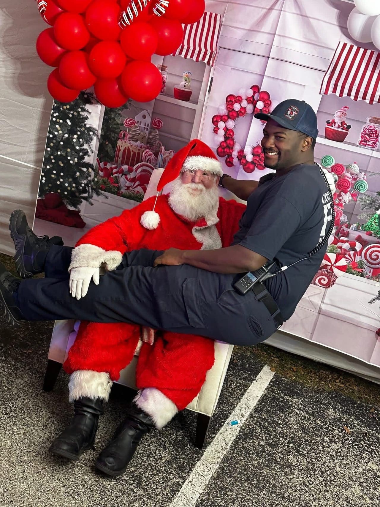 A smiling CHFD member sits on Santa's lap at a holiday photo booth decorated with red balloons and candy canes